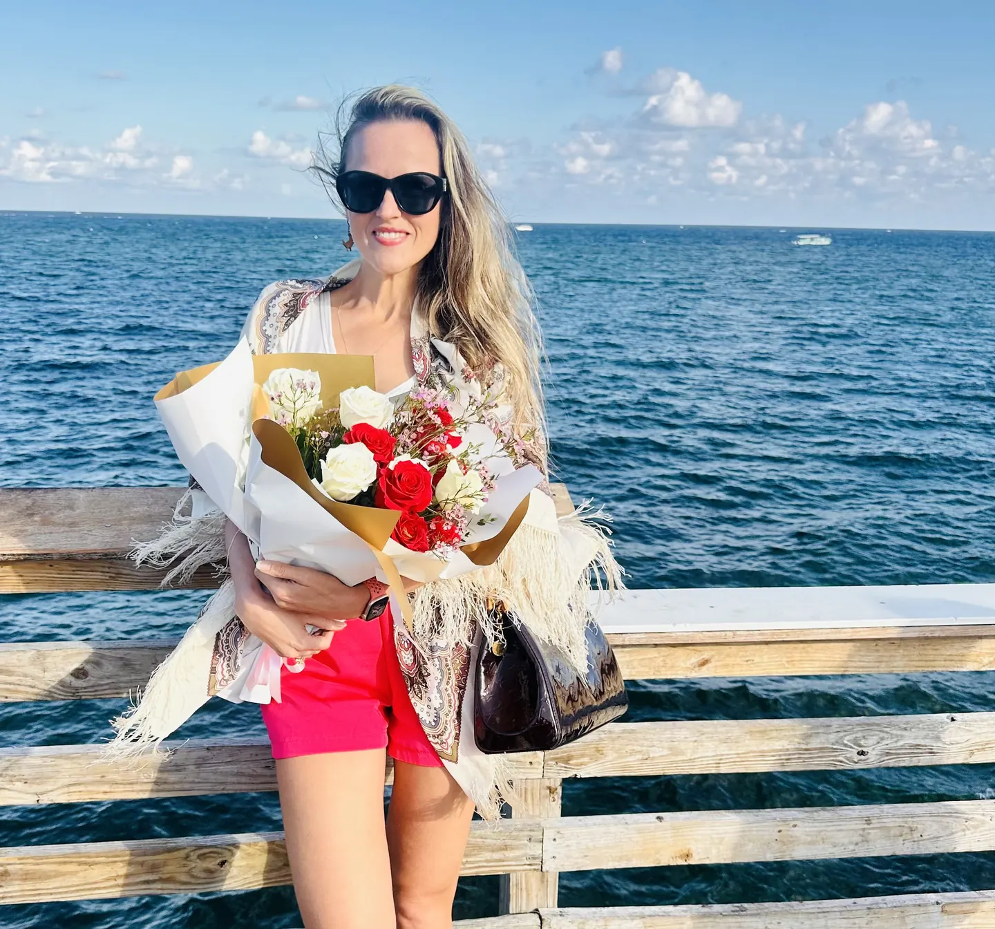 Maria smiling on a pier by the ocean, holding a bouquet of roses